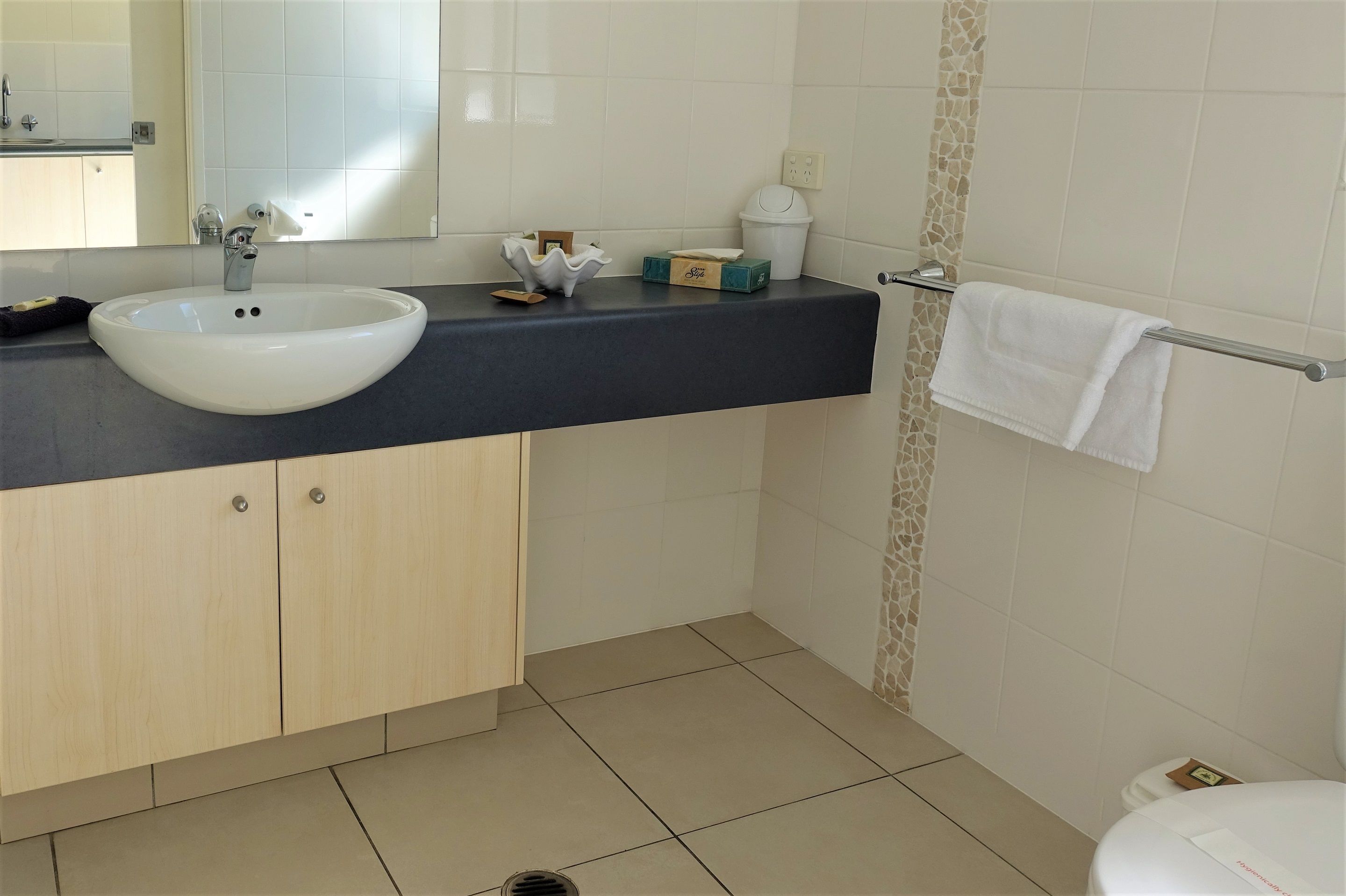 Un baño moderno con un lavamanos blanco, un espejo, un perchero para toallas y un inodoro.