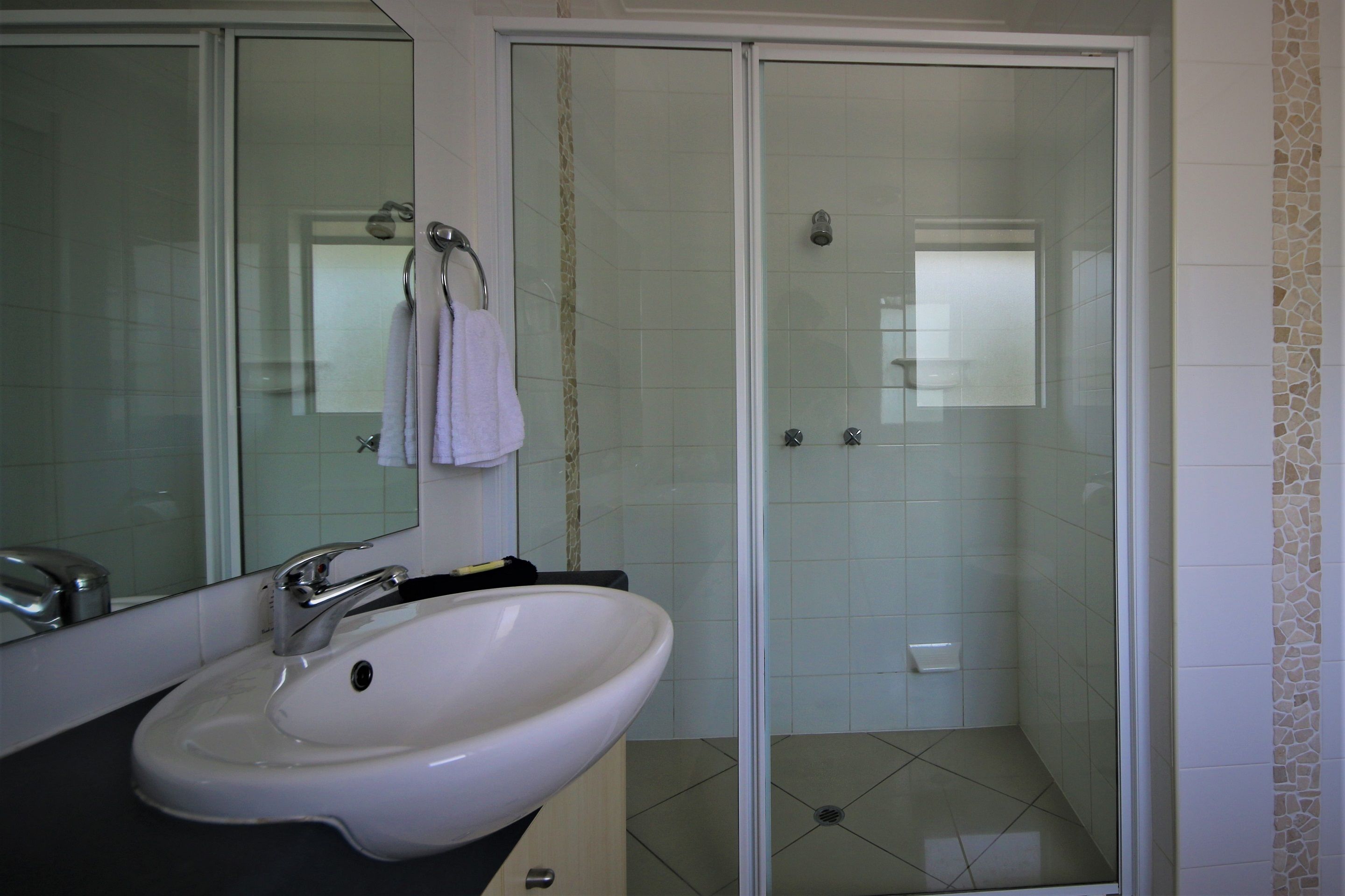 A bathroom with a white sink, a mirror, and a glass-enclosed shower.