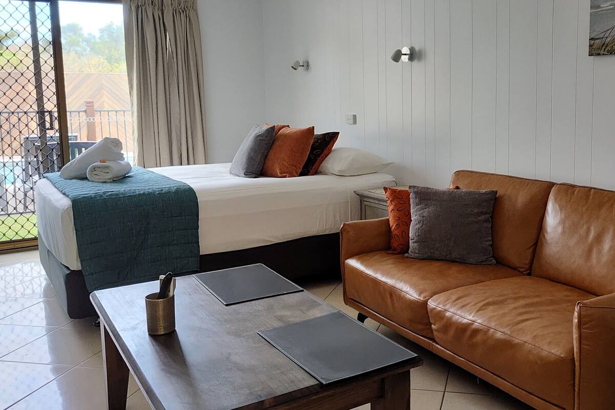 A hotel room with a bed, a brown leather sofa, a small table, and a window with curtains.