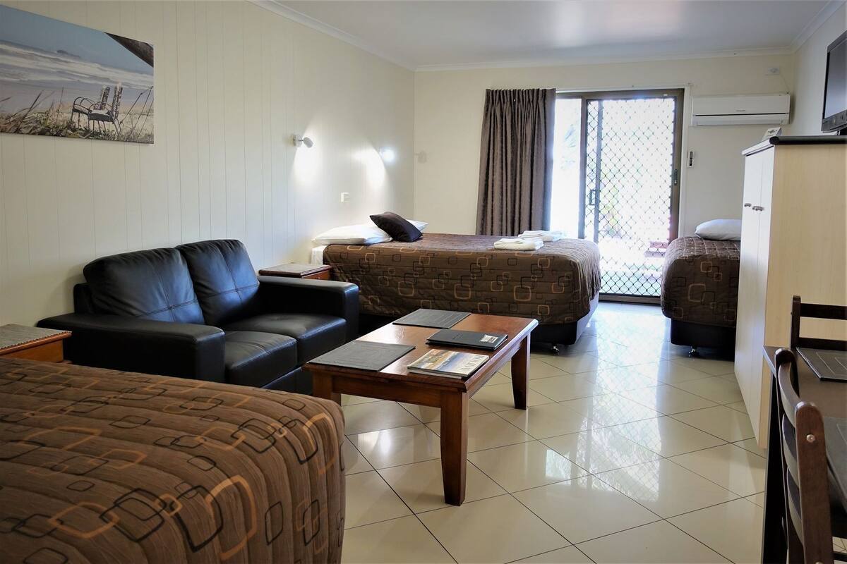 A hotel room with a sofa, a bed, a wooden table, and a TV.