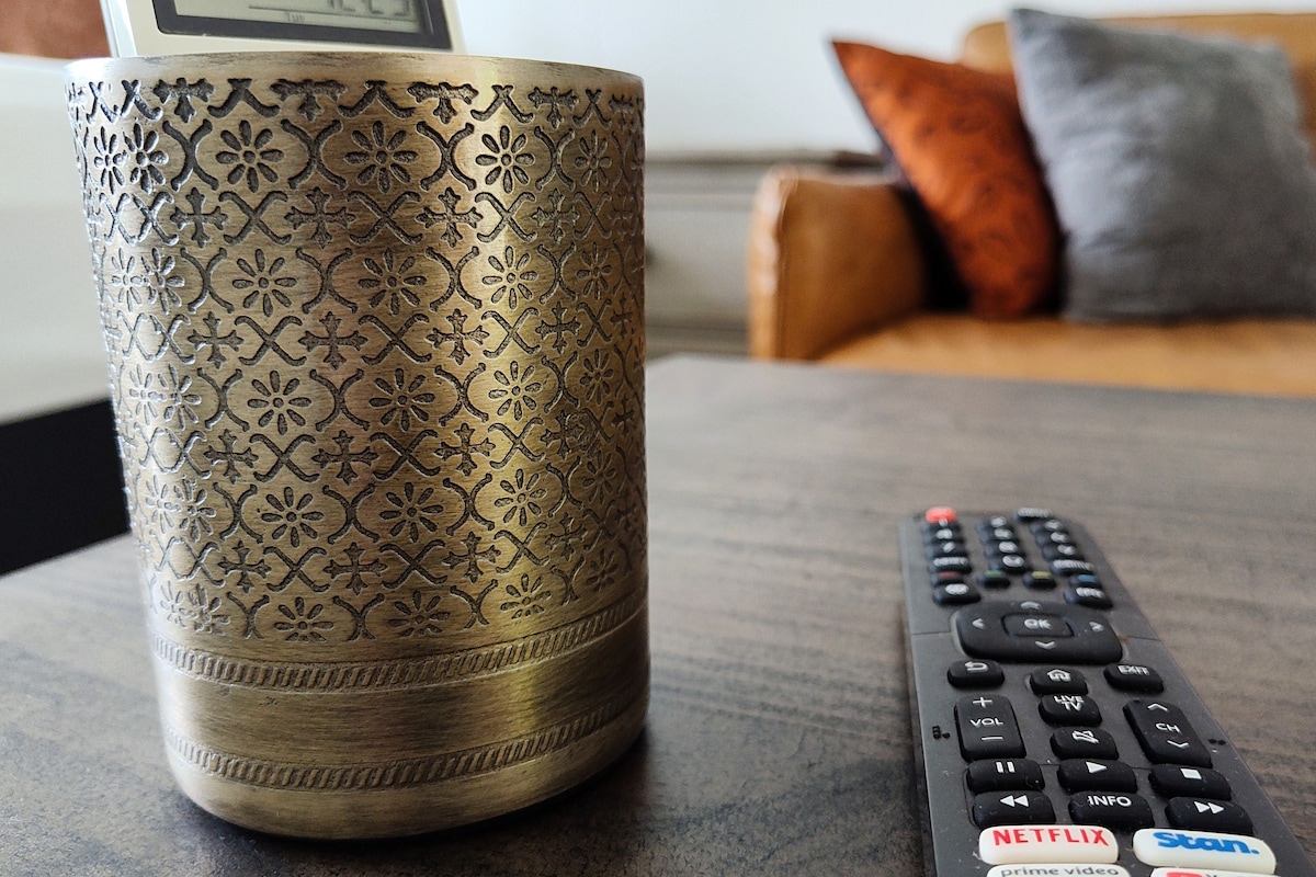 A remote control with buttons for Netflix, Prime Video, Stan, and YouTube, and a decorative vase on a table.