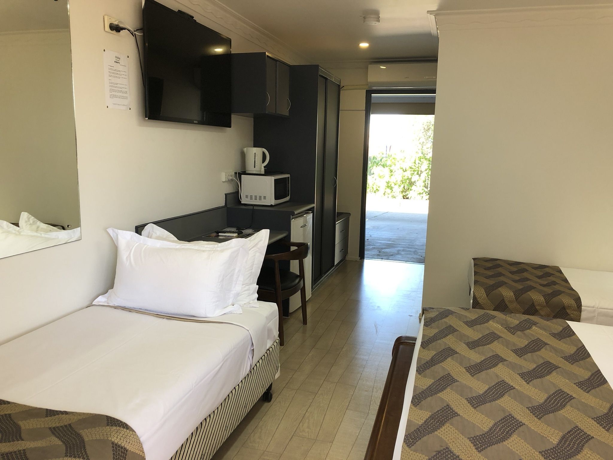 A hotel room with a bed, a desk with a microwave, and a view of the outdoors.