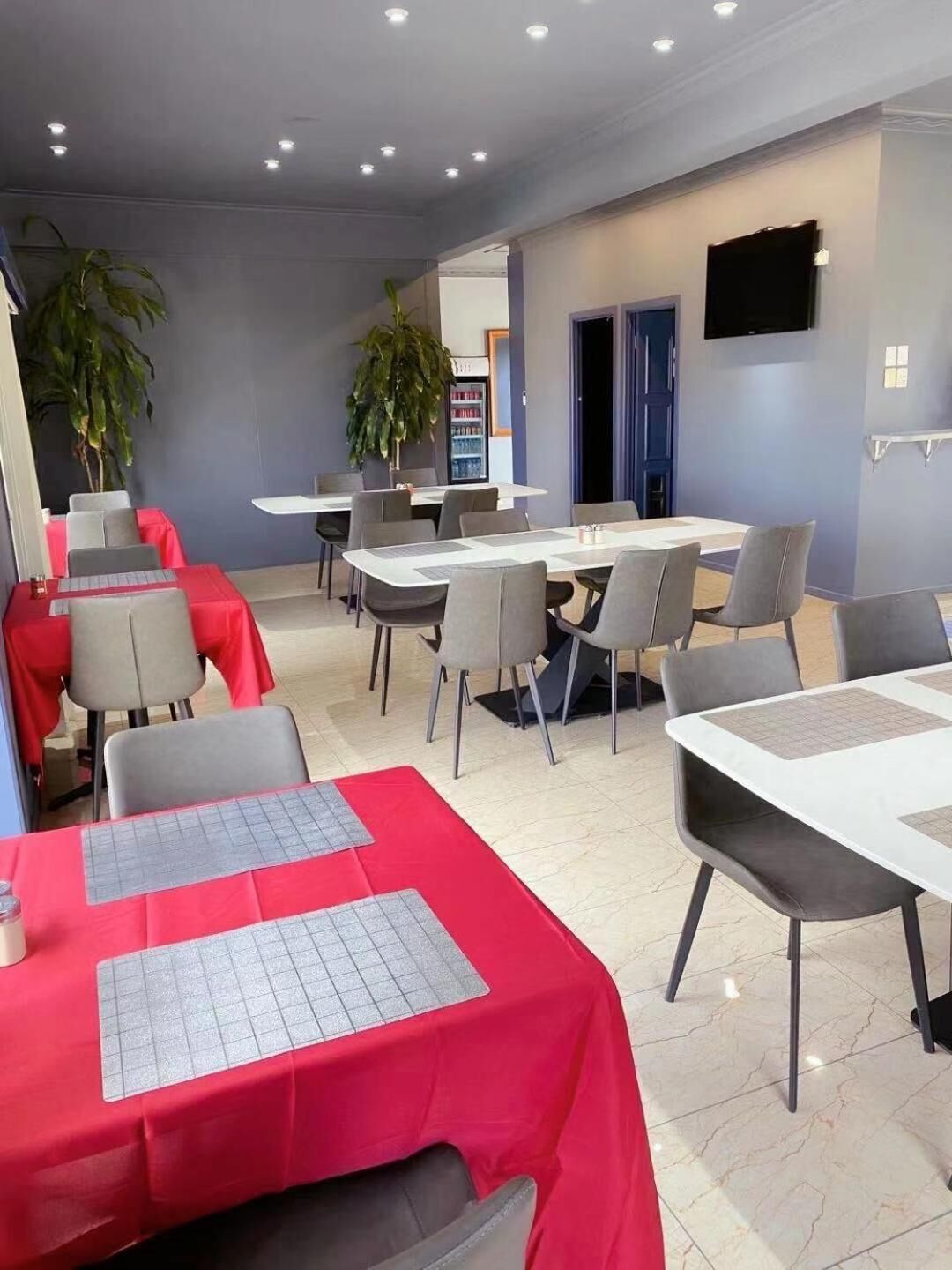 A dining area with tables and chairs, a refrigerator, and a television on the wall.