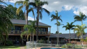 A resort with a swimming pool, palm trees, and a building with a balcony. - Oxley Motor Inn (Oxley)
