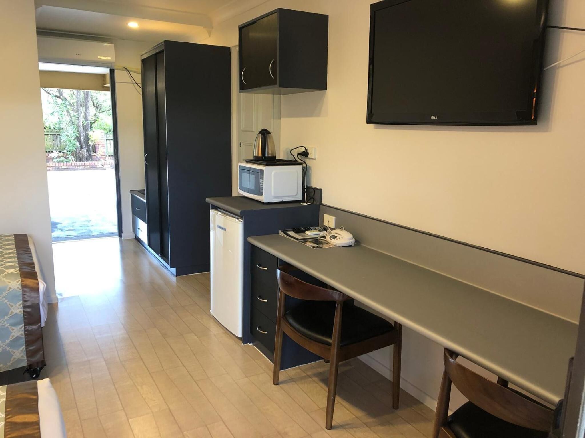 Una cocina compacta con microondas, un refrigerador pequeño y un televisor de pantalla plana montado en la pared.