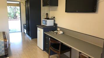Una cocina compacta con microondas, un refrigerador pequeño y un televisor de pantalla plana montado en la pared.