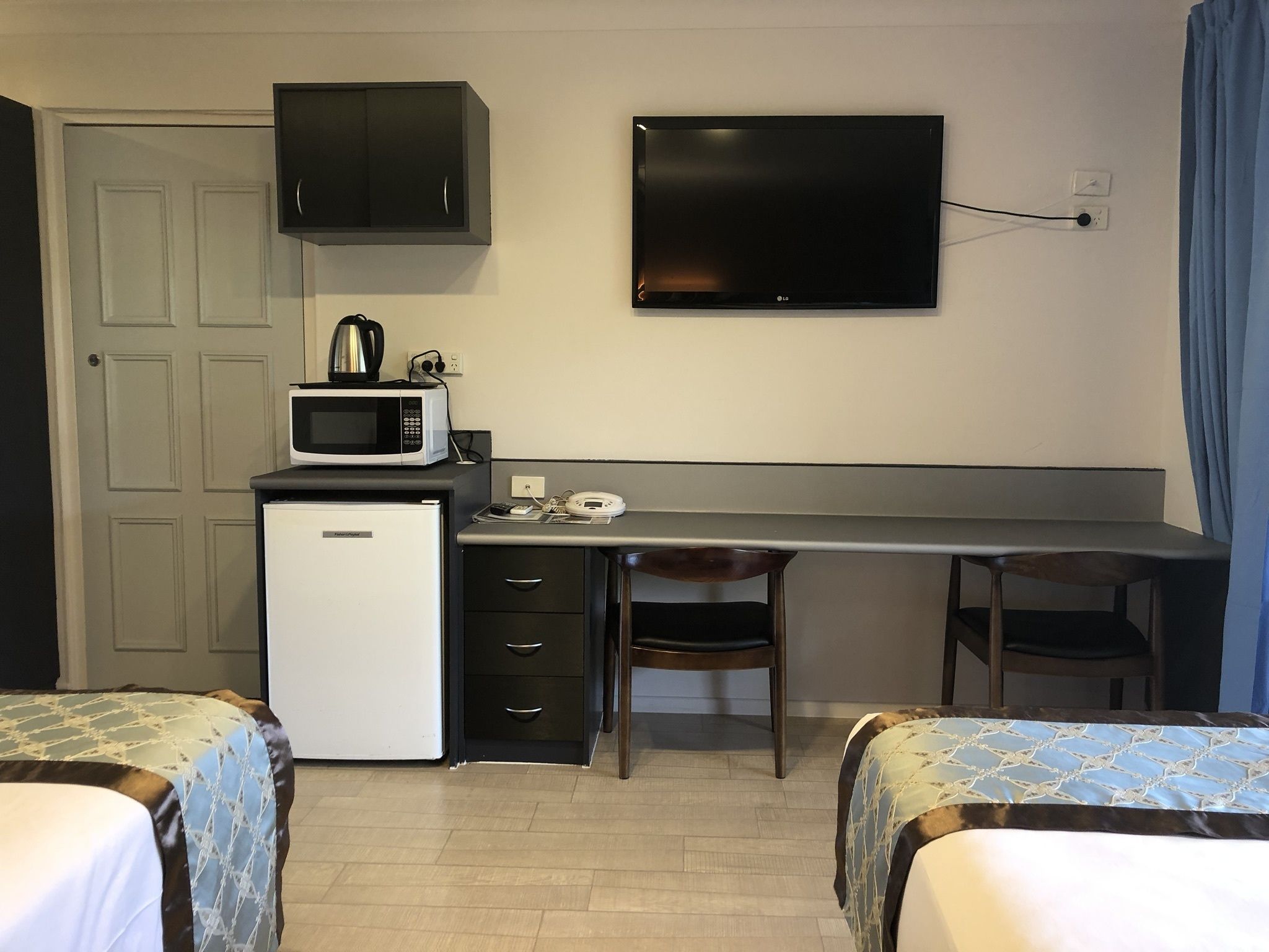 A compact room with a kitchenette, a flat-screen TV, two single beds, and a desk with a chair.