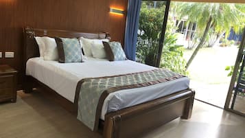 A hotel room with a large bed, wooden headboard, and a view of a garden through a sliding glass door.