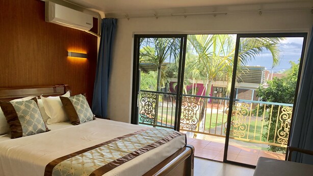 A hotel room with a large bed, a wooden headboard, a balcony with a view of palm trees and a building, and a table and chair in the corner. - Oxley Motor Inn (Oxley)