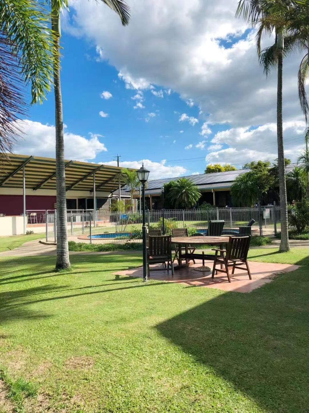 An outdoor patio area with a table and chairs, surrounded by palm trees and a covered seating area.
