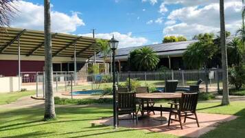 An outdoor patio area with a table and chairs, surrounded by palm trees and a covered seating area.