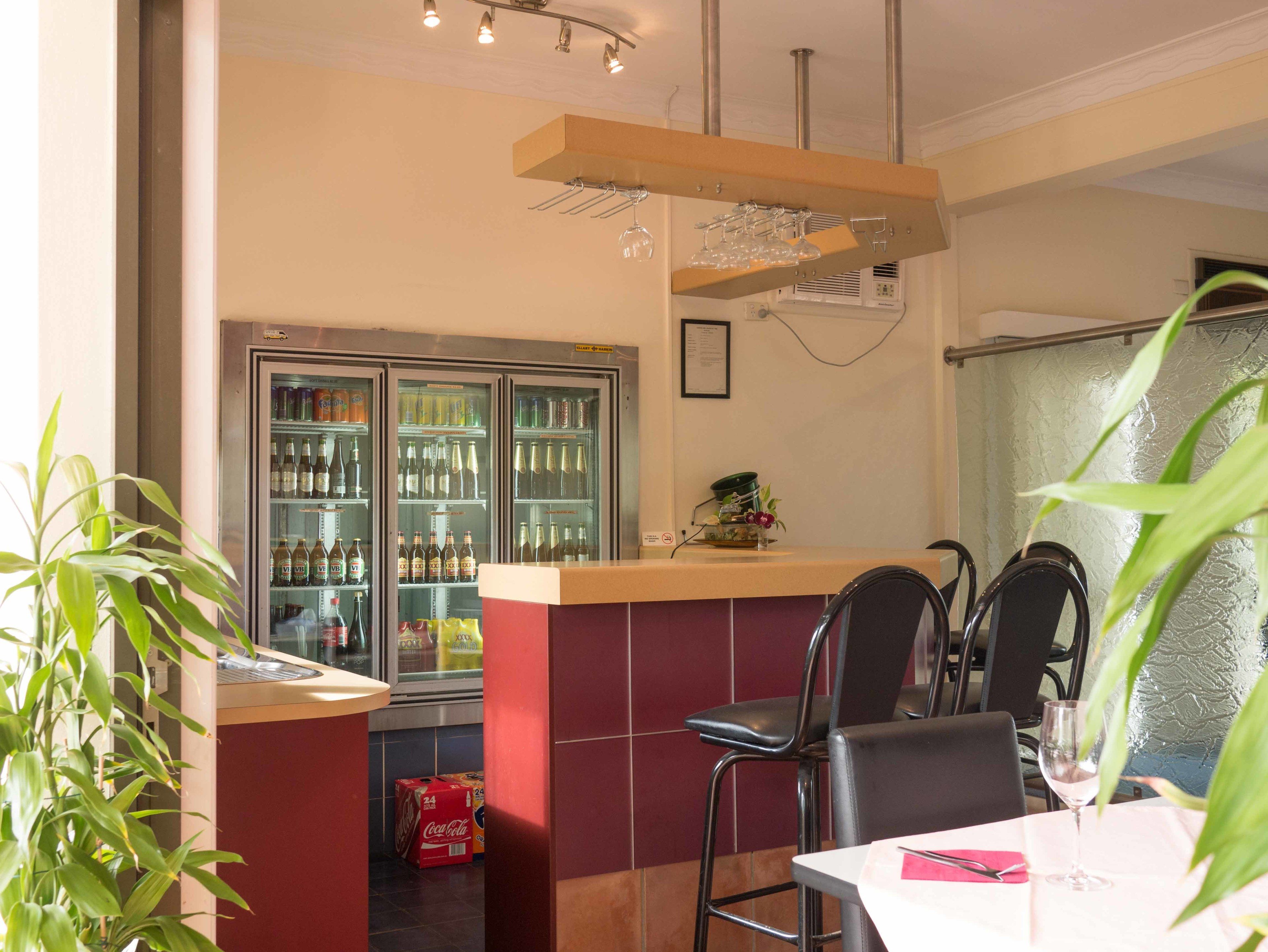 Een restaurantinterieur met een bar, zitplaatsen en een drankkoelkast.