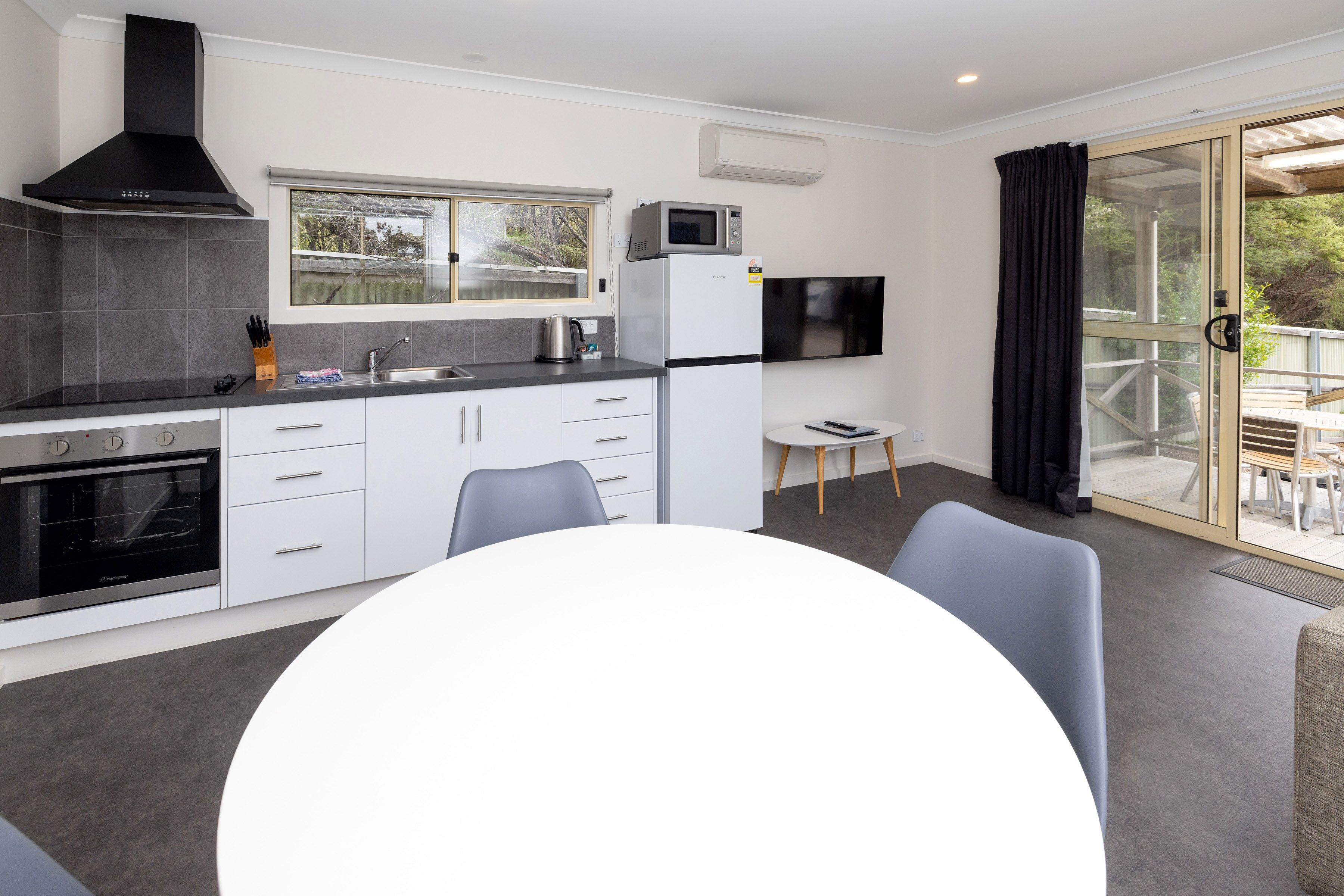 Una cocina moderna con armarios blancos, una estufa negra y un microondas. Hay una mesa de comedor con sillas y una mesita con un control remoto.