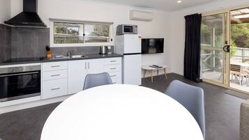 Una cocina moderna con armarios blancos, una estufa negra y un microondas. Hay una mesa de comedor con sillas y una mesita con un control remoto.
