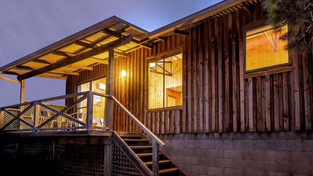 Una cabaña de madera con un porche cubierto, una escalera y un gran ventanal.