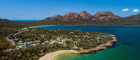 An aerial view of a coastal area with a beach, a small settlement, and mountains in the background.