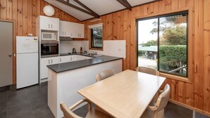 Cocina compacta con armarios blancos, un microondas y un lavamanos. Hay una mesa de madera con cuatro sillas.