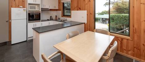 A compact kitchen with white cabinets, a microwave, and a sink. There is a wooden dining table with four chairs.