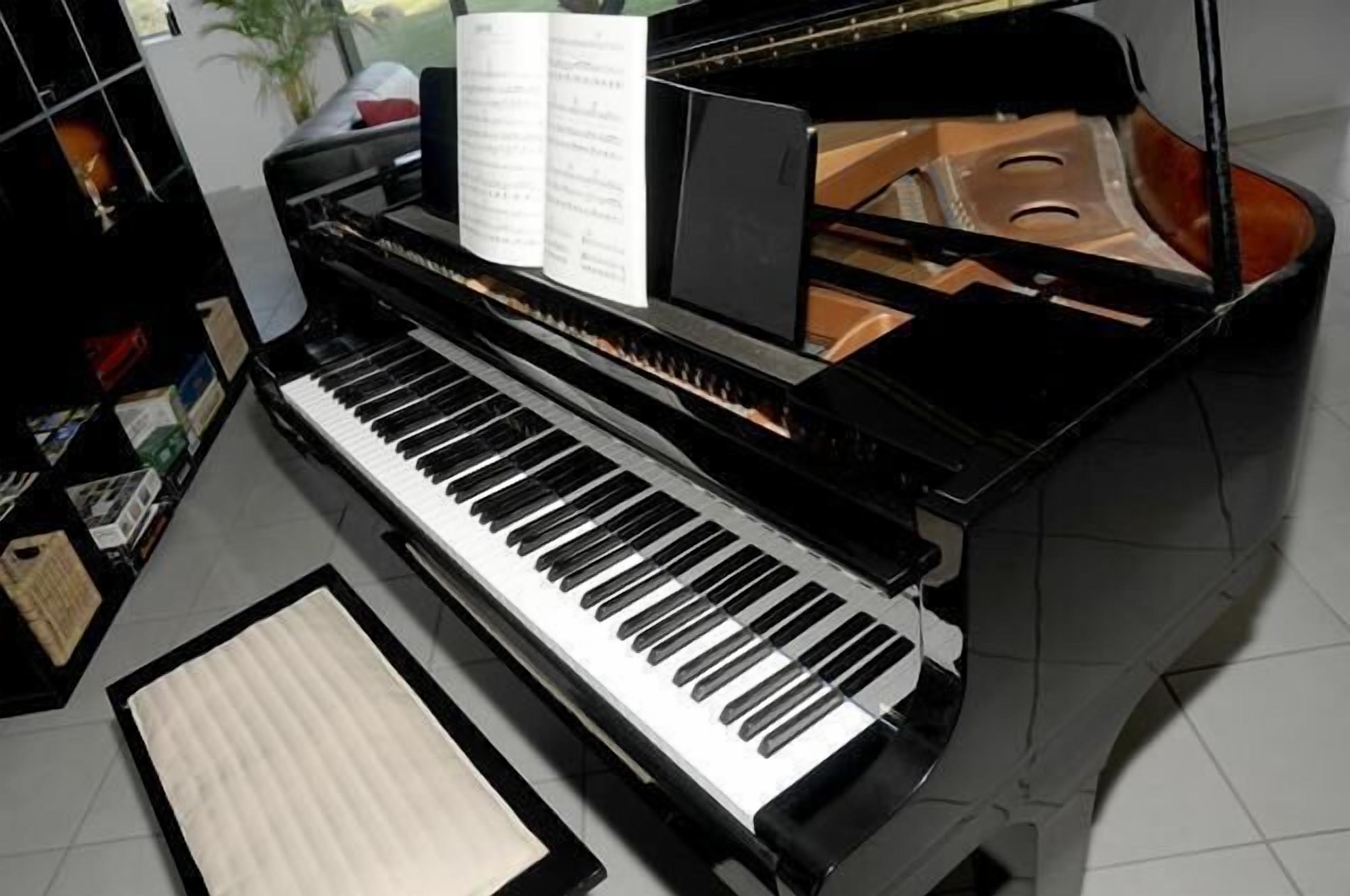 A grand piano with sheet music on the stand, a music stand, and a music rest on the floor.