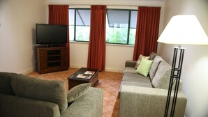 Ein Wohnzimmer mit Flachbildfernseher, Couchtisch, Sofa und Stehlampe.