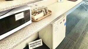 Eine Küchenzeile mit Mikrowelle, Toaster, Wasserkocher und einer kleinen Pflanze. Ein Schild weist auf kostenloses Internet hin und eine Notiz bittet darum, die Schuhe auszuziehen.