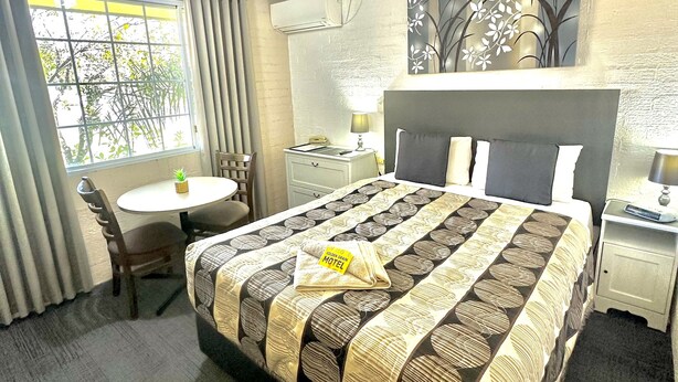 Ein Hotelzimmer mit Bett, Schreibtisch, Stuhl, einem Fenster mit Vorhängen, einer Klimaanlage und einem Deckenventilator.