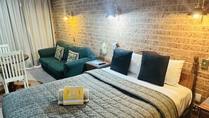 Ein gemütliches Hotelzimmer mit Backsteinwand, einem großen Bett mit Steppdecke, einem grünen Sofa und einem weißen Sessel.