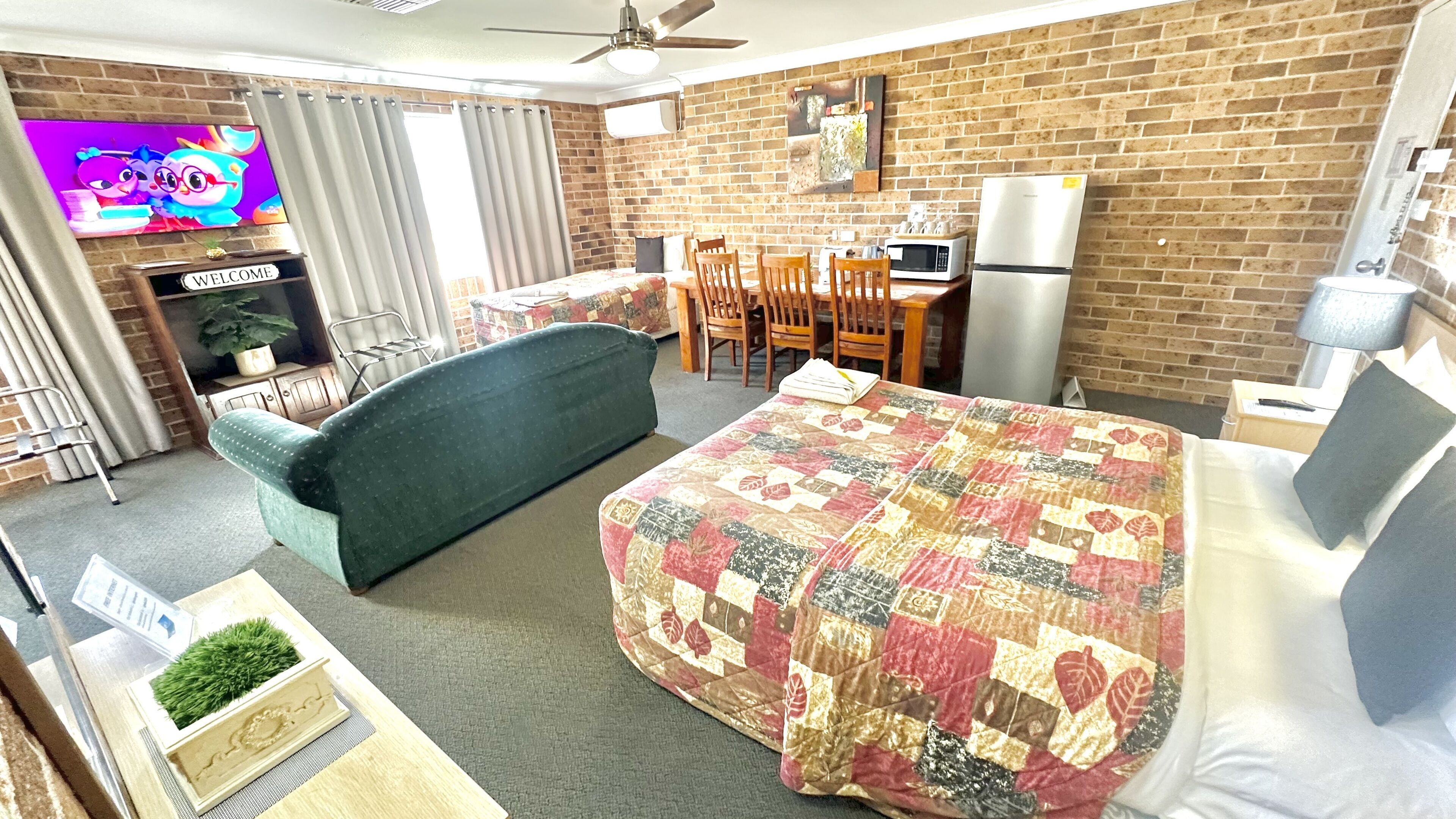 Habitación de hotel con cama, sofá, televisión, mesa de comedor con sillas, microondas y refrigerador.