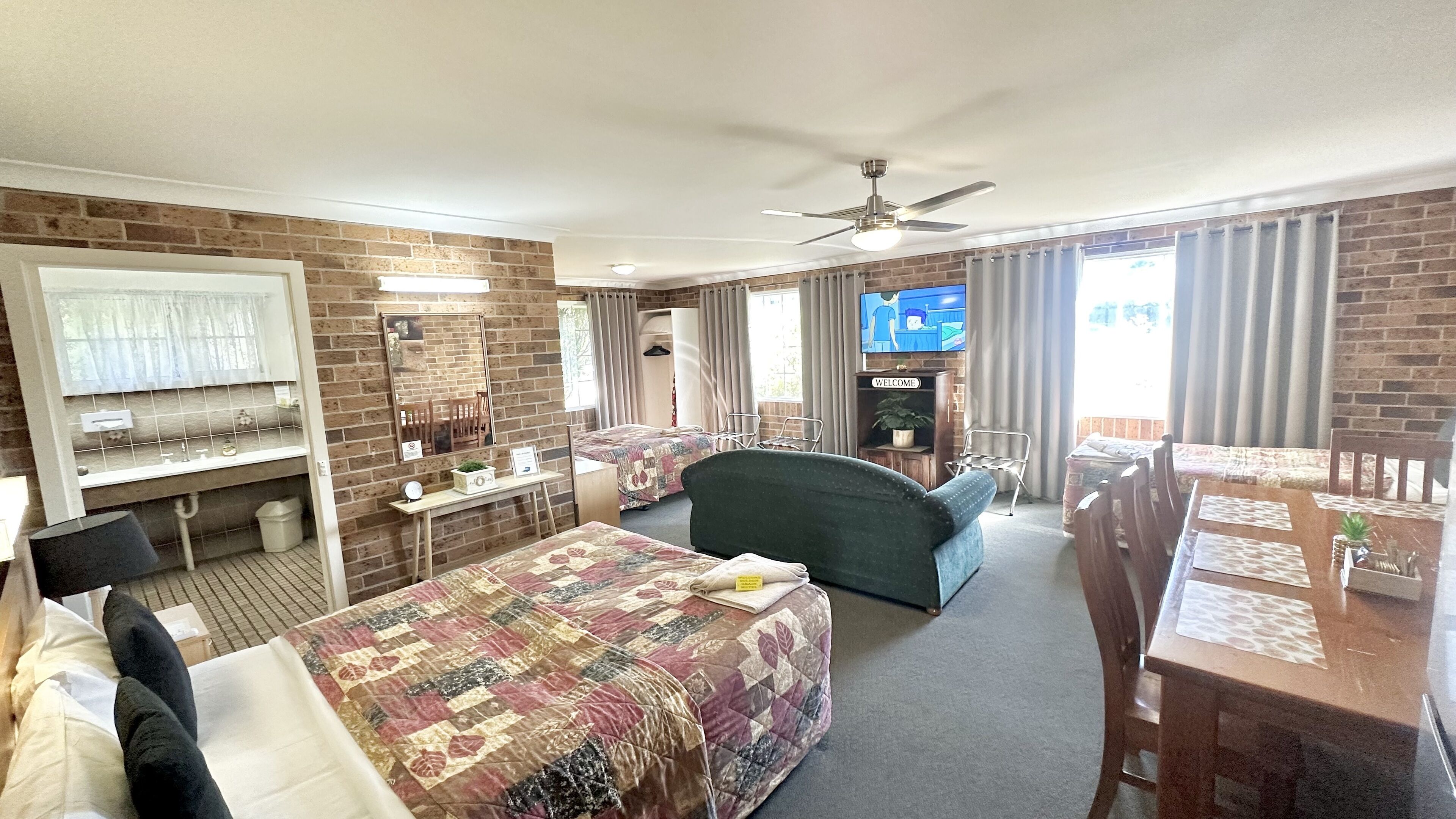 A hotel room with two beds, a TV, a ceiling fan, and a brick wall.