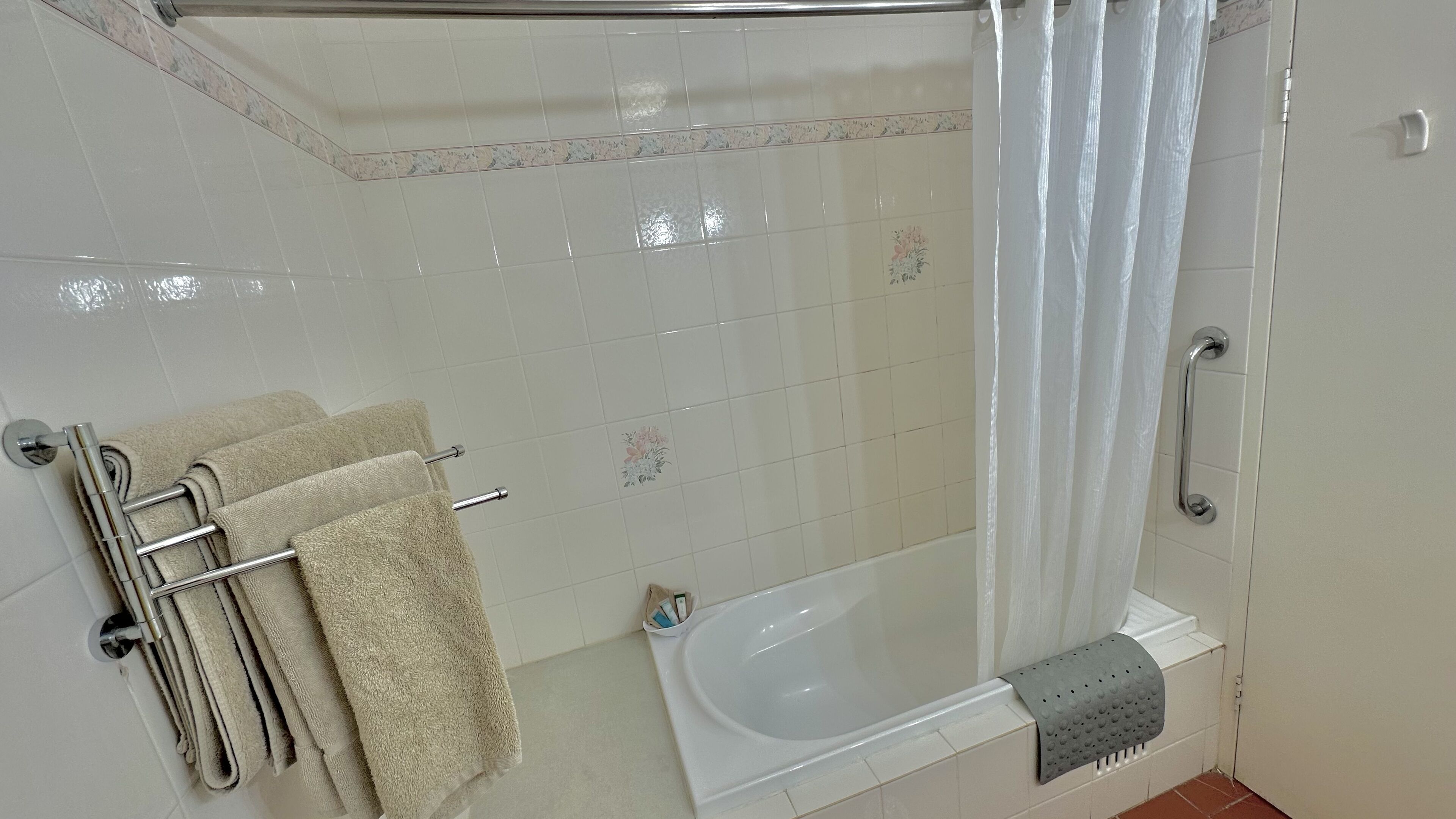 A bathroom with a bathtub, a shower curtain, and a towel rack with towels.