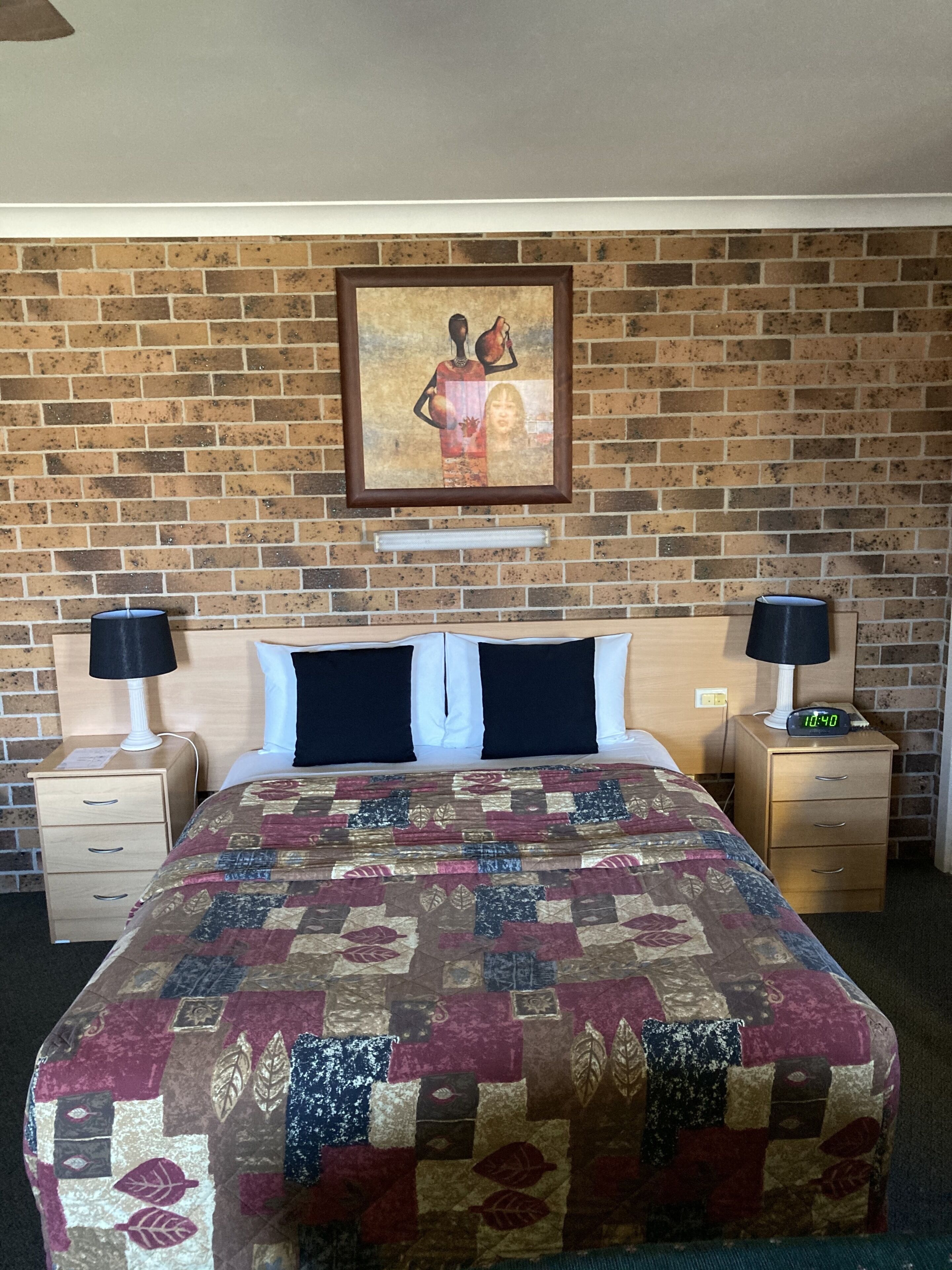 Una camera d'albergo con un muro in mattoni, un letto con copriletto, due comodini con lampade e un quadro sopra il letto.