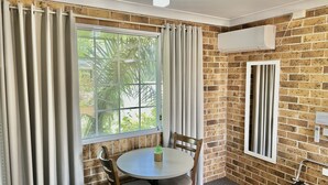 Ein Zimmer mit Backsteinwand, einem fenster mit Vorhängen, einem runden Tisch mit Stühlen und einer Klimaanlage.