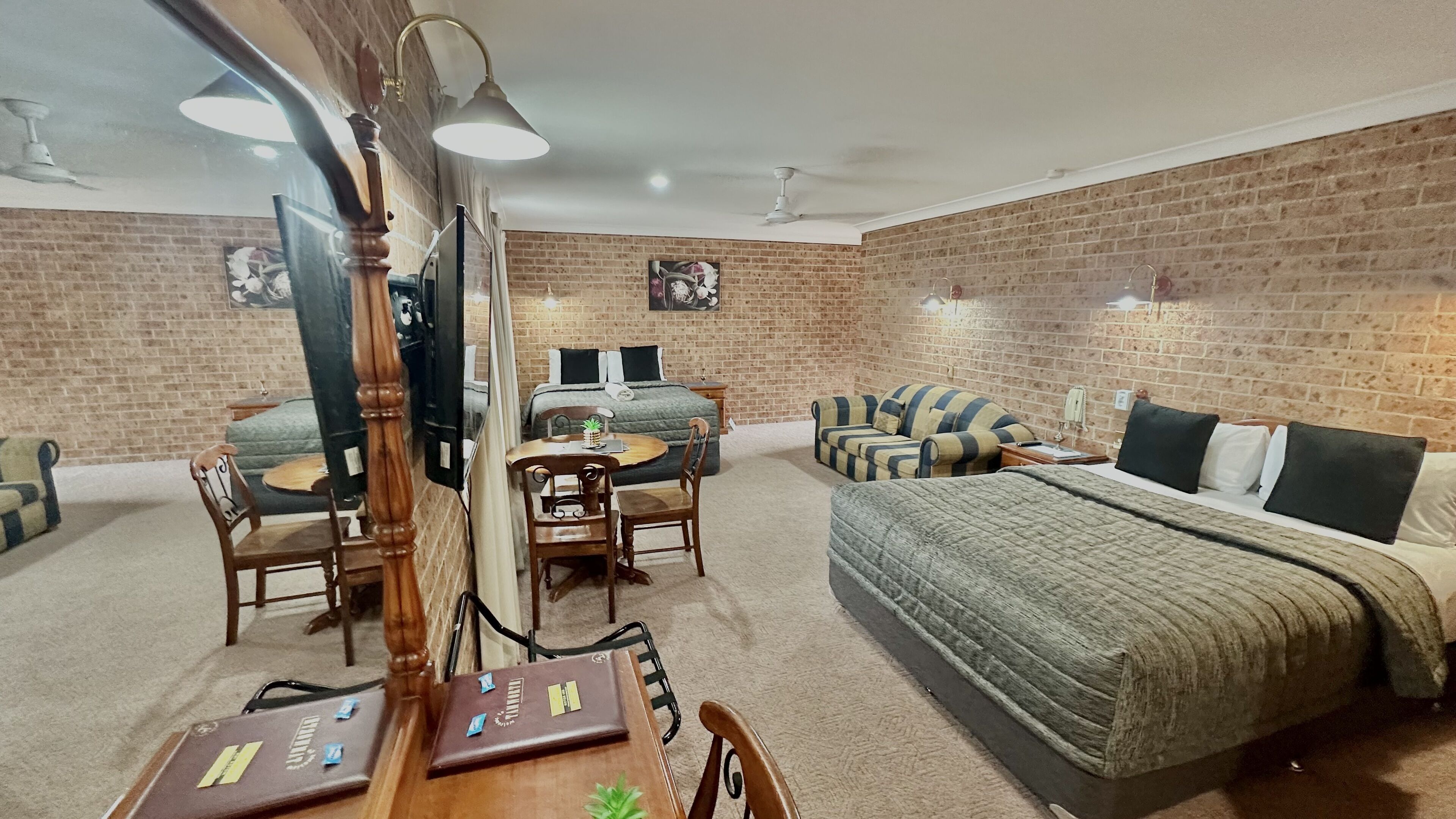 Una habitación con pared de ladrillo, cama, sofá, mesa de comedor con sillas y televisor.