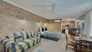 Ein Zimmer mit Backsteinwand, einer Couch, einem Bett, einem Schreibtisch mit Stuhl und einem Deckenventilator.