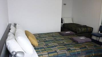 A hotel room with a bed, a chair, and a desk with a lamp.