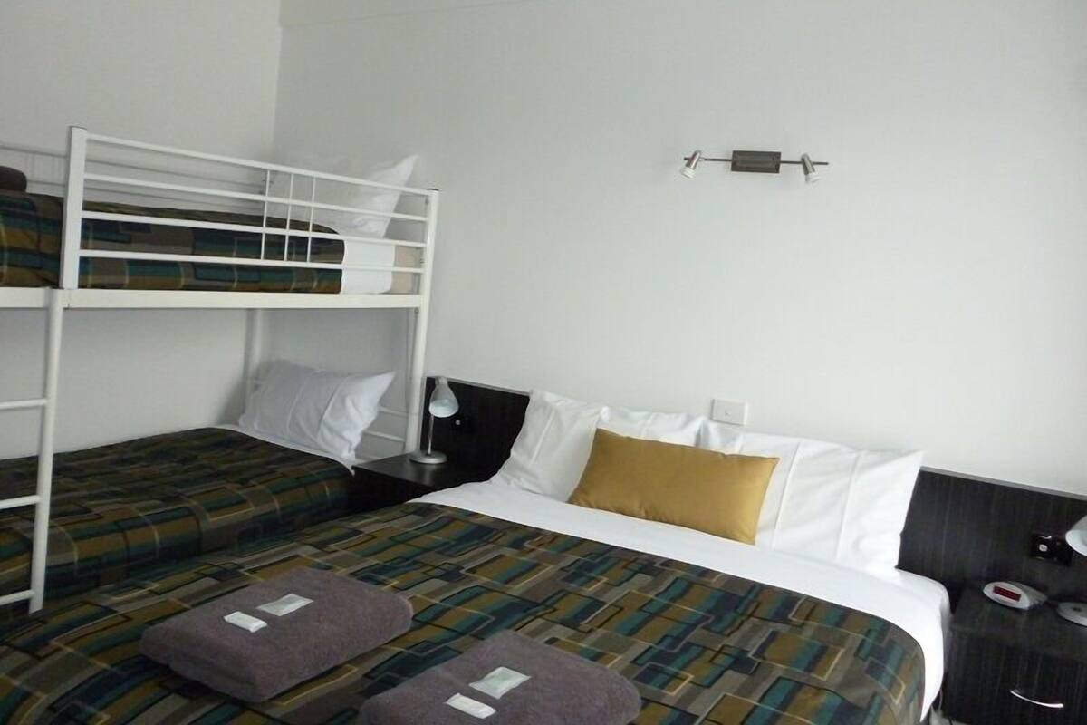 Une chambre d’hôtel avec un lit superposé, un lit simple, une table de chevet avec une lampe et une petite table de nuit avec un téléphone.