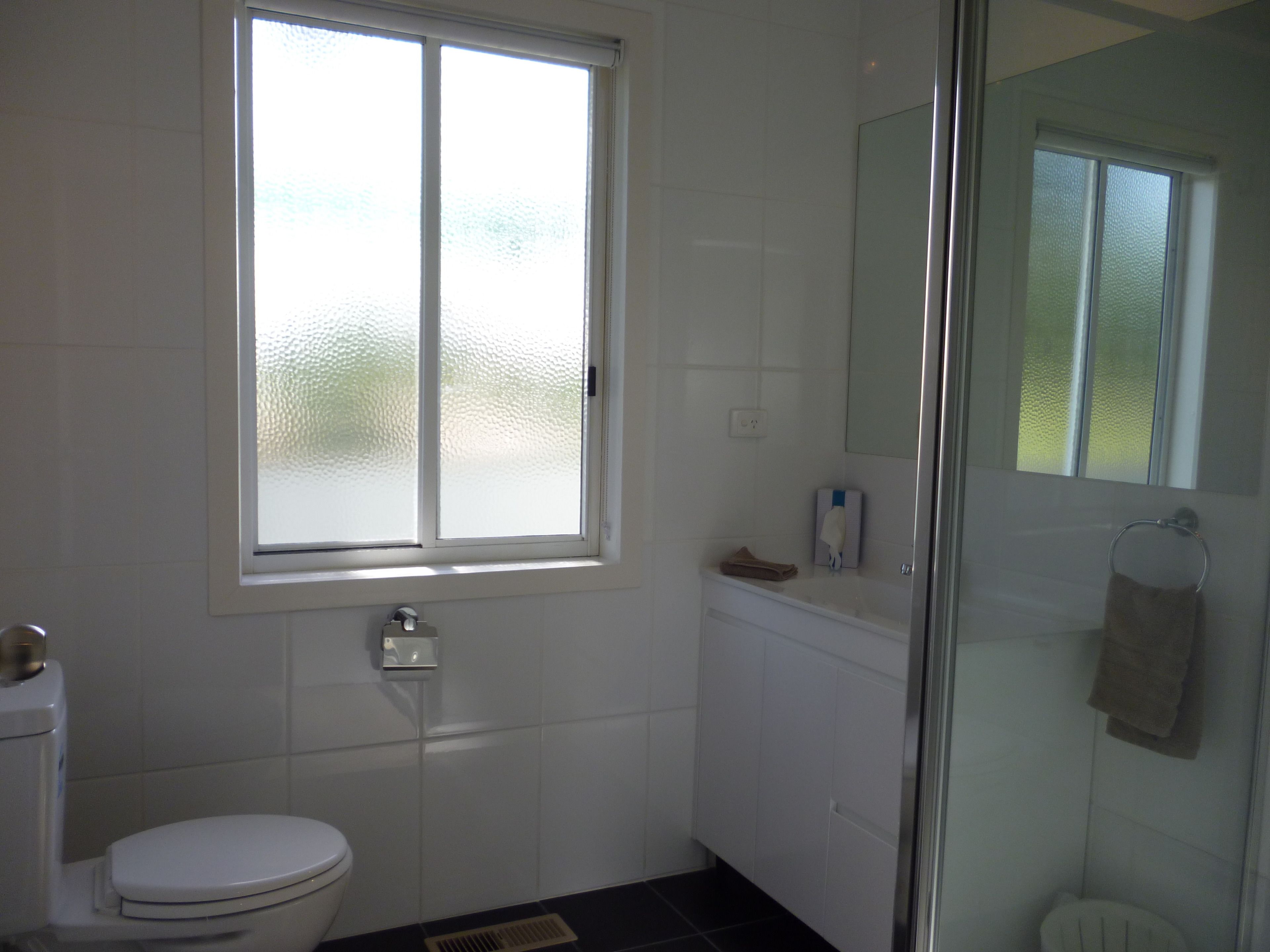Een badkamer met toilet, een raam, een douche en een handdoekhouder.
