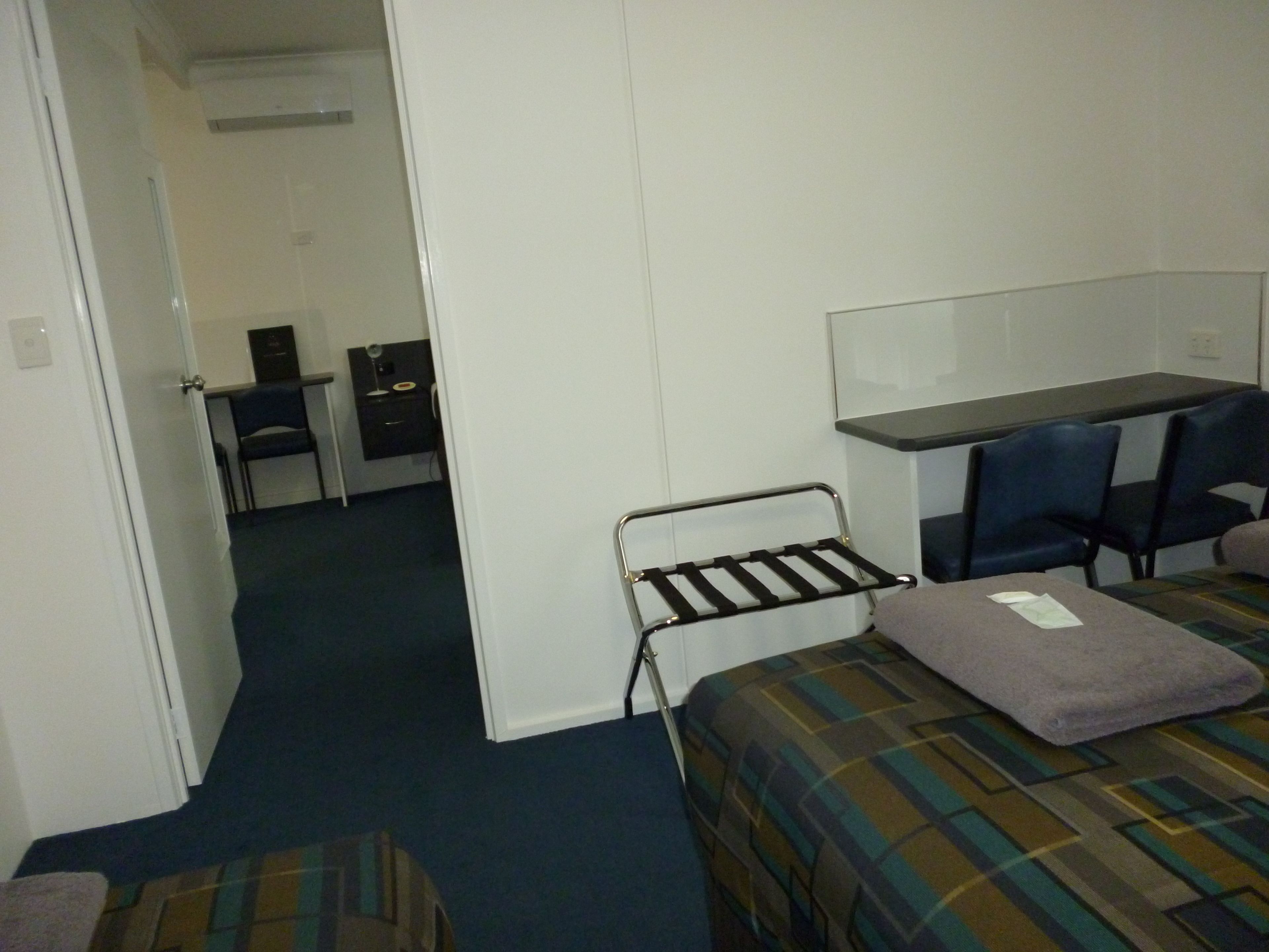 Quarto de hotel com uma cama, uma escrivaninha e duas cadeiras.