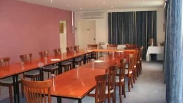 Un salón de conferencias con una larga mesa, sillas, una pizarra blanca y un equipo de aire acondicionado.