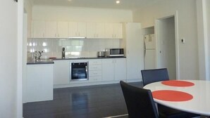 Una cocina moderna con armarios blancos, microondas y lavavajillas. Hay una mesa de comedor con sillas y un detalle rojo sobre la mesa.
