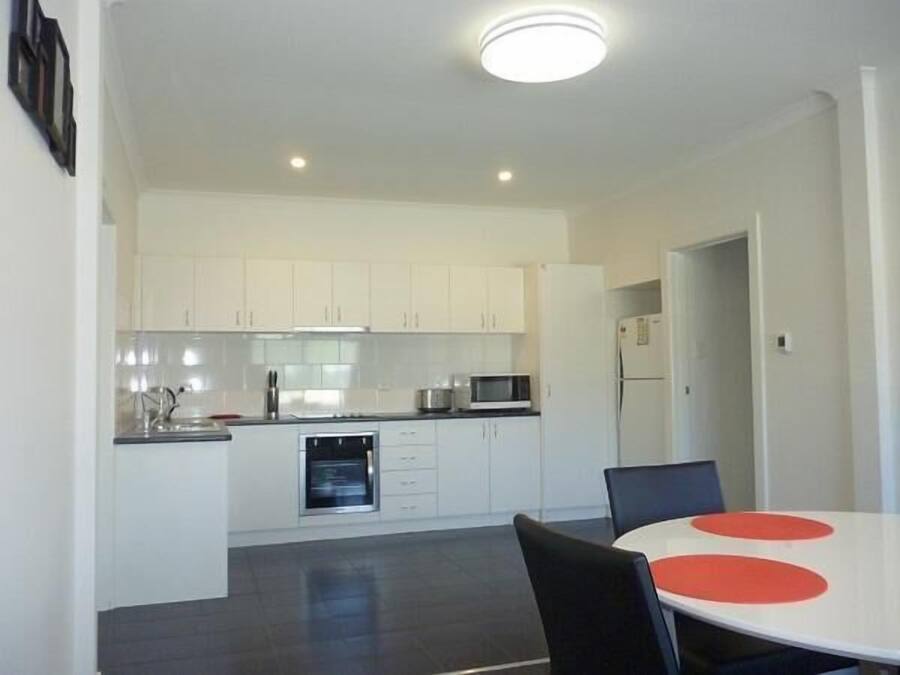 Una cocina moderna con armarios blancos, microondas y lavavajillas. Hay una mesa de comedor con sillas y un detalle rojo sobre la mesa.