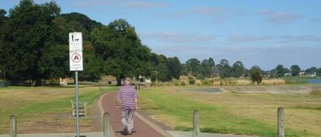 A person walking on a paved path in a park with a sign indicating camping is prohibited.