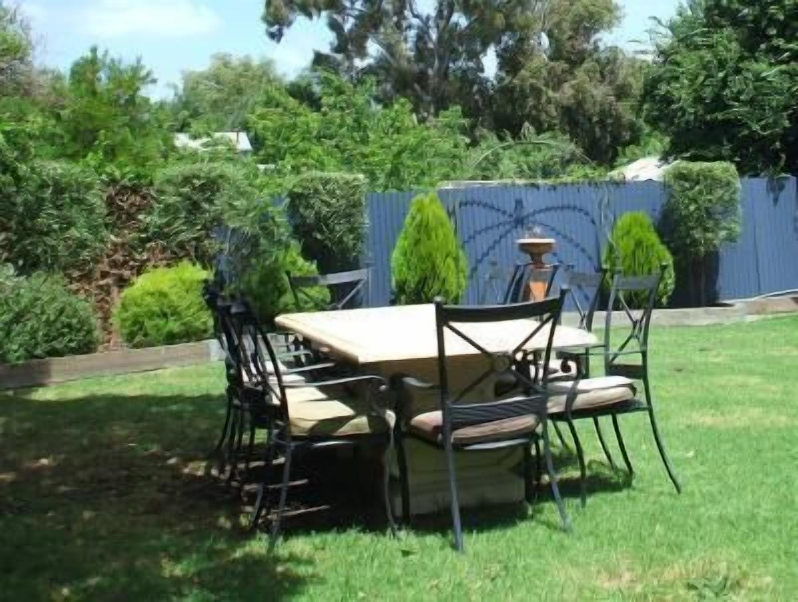 Un patio al aire libre con una mesa y sillas, rodeado de follaje y una cerca azul.