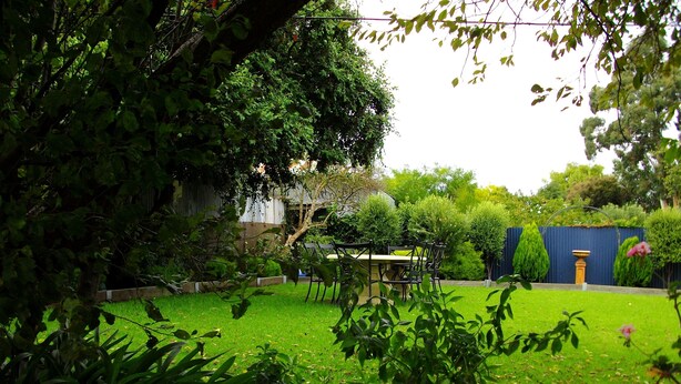 Un jardín bien cuidado con un área de comedor, rodeado de abundante vegetación y una cerca azul.