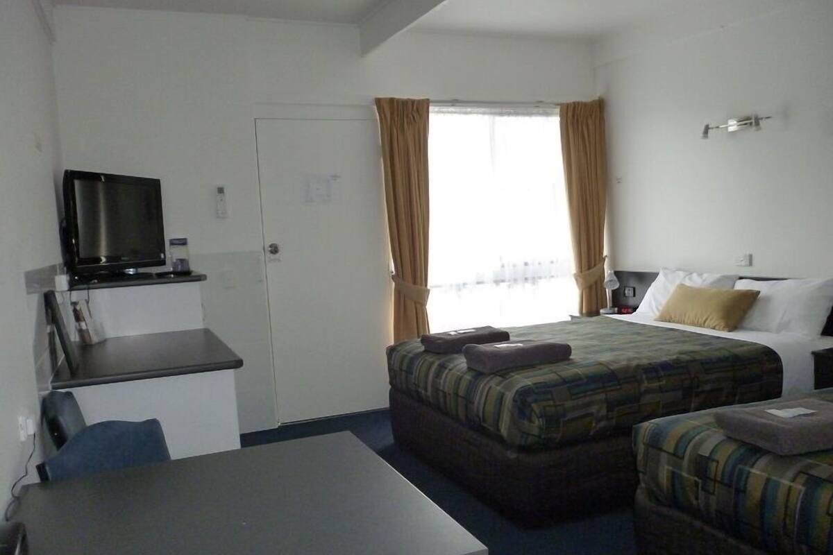 Une chambre d’hôtel avec un lit, un bureau, une télévision et une fenêtre avec des rideaux.