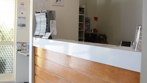Un mostrador de recepción con encimera blanca y paneles de madera, un tablón de anuncios y una puerta de cristal que da al exterior.