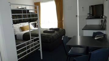A compact room with bunk beds, a small table, chairs, a television, and a window with curtains.