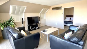 A spacious living room with a large black leather sofa, a coffee table, and a flat-screen TV. - Alpha Motel Christchurch (Christchurch)