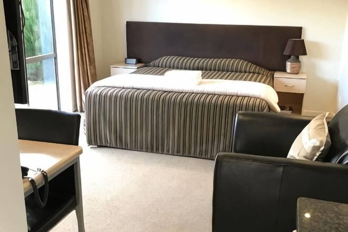 Une chambre d’hôtel comprenant un lit, un bureau, une chaise, une table de chevet et une lampe.