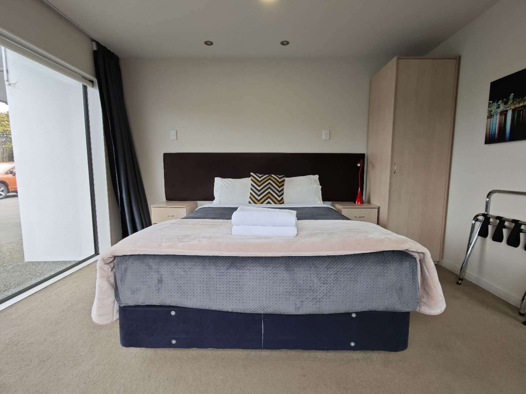 A bedroom with a bed, two bedside tables, a wardrobe, and a door leading to a balcony.